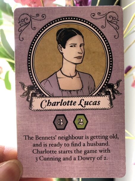 The Charlotte Lucas card from the game Marrying Mr. Darcy. There is a portrait of Charlotte Lucas in a purple dress with an analytical look on her face. The card says, "The Bennets' neighbor is getting old, and is ready to find a husband. Charlotte starts the game with 3 Cunning and a Dowry of 2.
