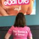 In front of the Barbie movie poster, with a t-shirt that says "This Barbie is a writer" on the back