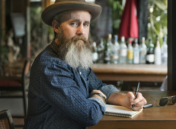 A hipster writer. He looks at you instead of his page. He might be pensive, but he might be sadness. Perhaps writing requires a certain weight of sadness, at least in 2023.